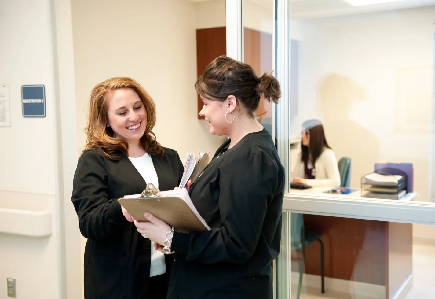 Two Novant Health team members are holding clipboards full of information as they stand outside of an office. 