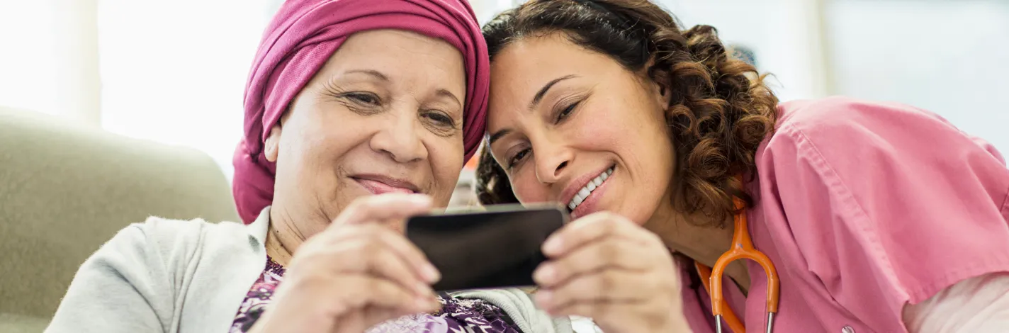 Nurse sitting with a cancer patient as they look at the patient's smartphone together. 