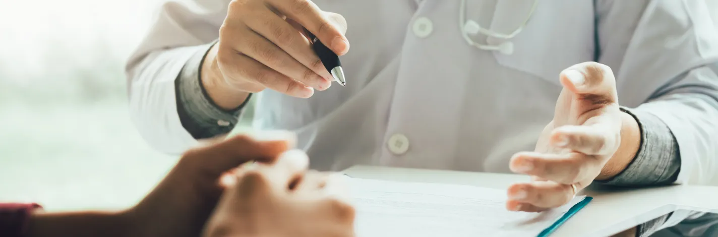 Photo of physician's hands holding a pen across from another person