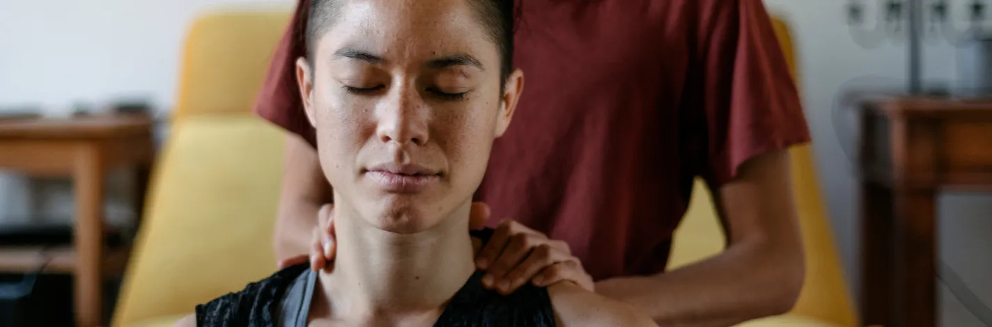 Couple in their home. The woman in sitting on the floor while her partner is sitting behind her massaging her shoulders. 