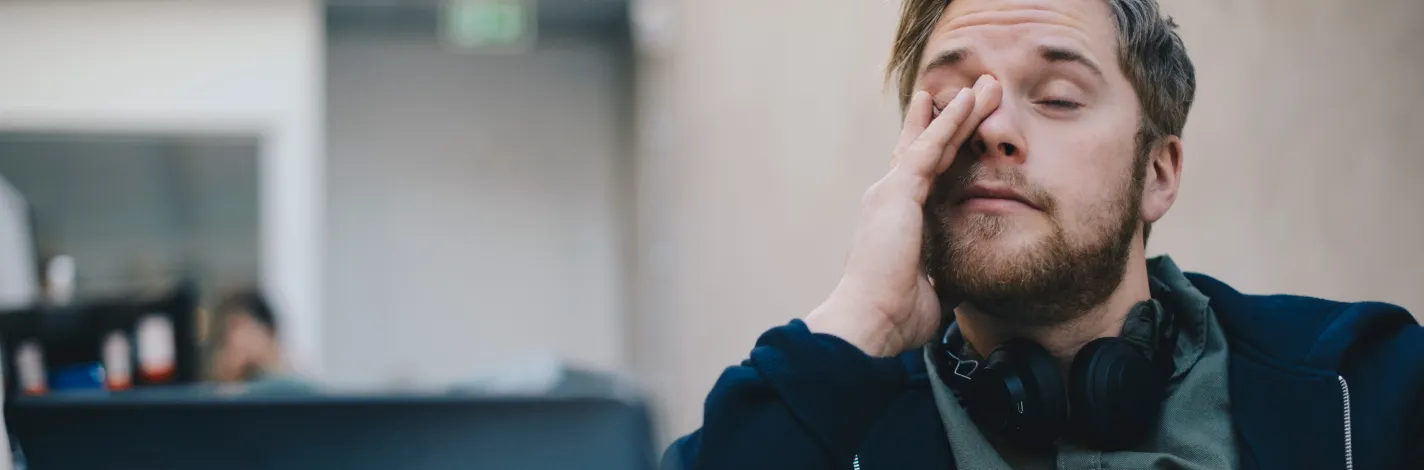 Photo of a tired man in front of laptop rubbing his eyes