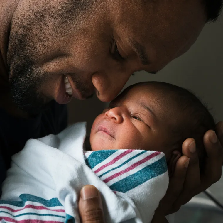 A swaddled newborn being held by father