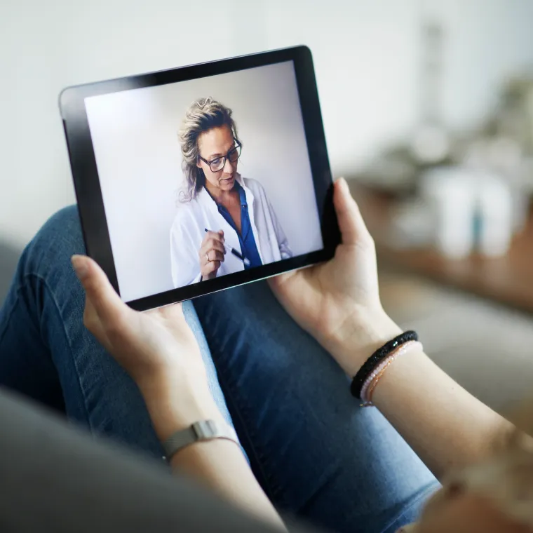 A patient is holding an iPad in their lap with their doctor on the screen during a virtual visit.