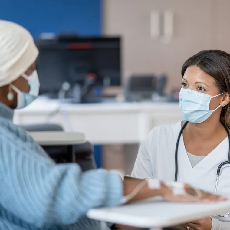 A masked nurse and patient are sitting across from each other talking as treatment is being prepared. A masked nurse and patient are sitting across from each other talking as treatment is being prepared.