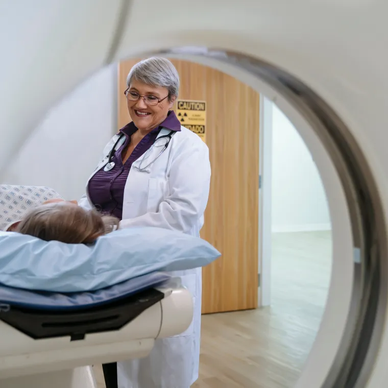A doctor is talking with a patient as they lie down preparing for an imaging scan. 