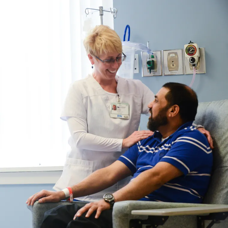 A Novant Health nurse is standing next to a male patient as they smile at one another and prepare for infusion treatment