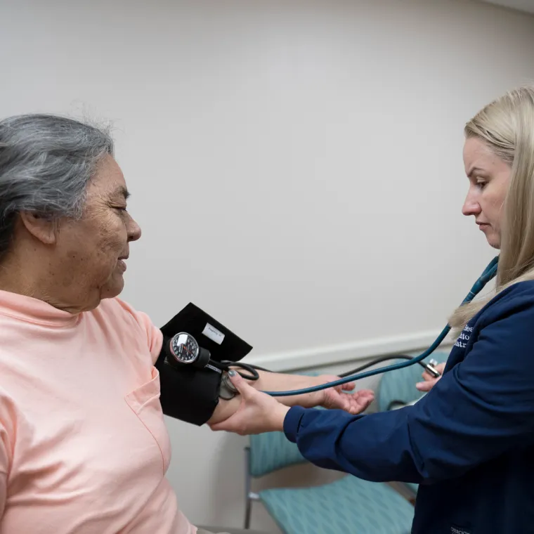 A Novant Health nurse is taking the blood pressure of a senior woman as she sits on an exam table. 