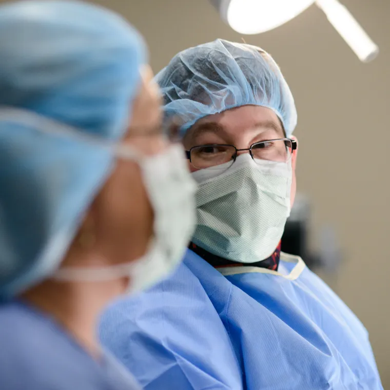 A Novant Health team member is dressed in personal protective equipment (PPE) looking over at another team member during surgery.. 