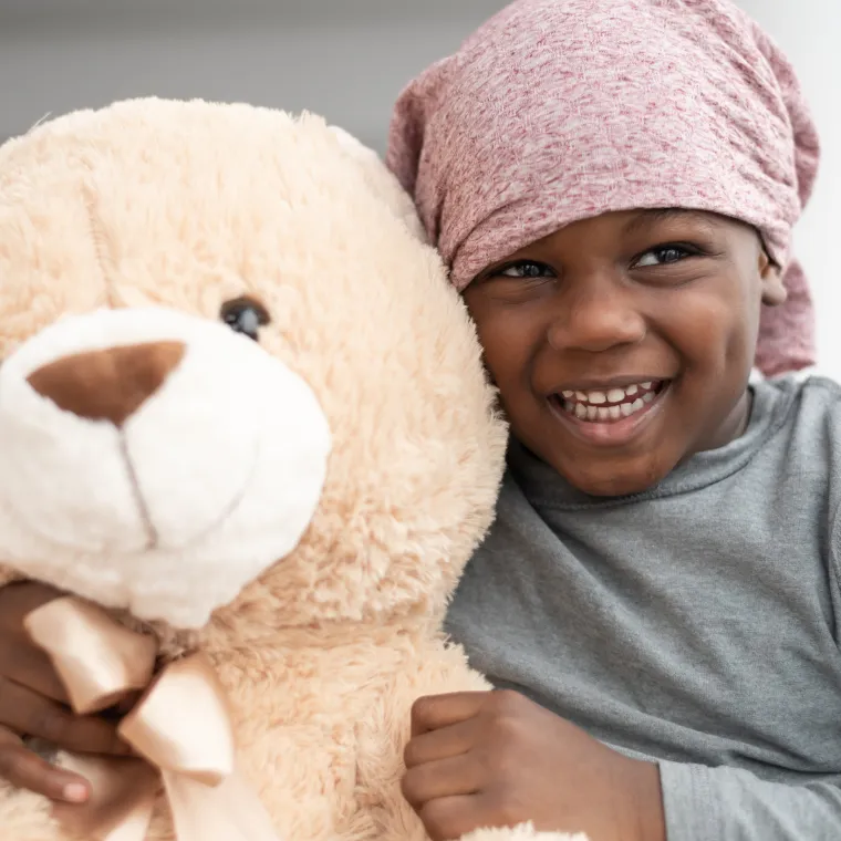 Young child wearing is wearing a head wrap and hugging a teddy bear. Young child wearing is wearing a head wrap and hugging a teddy bear.