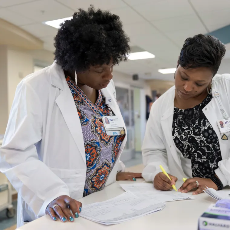 Two Registered Nurses reviewing and filling out forms at a counter in the hospital. 