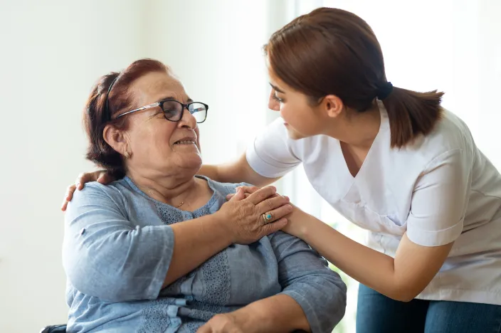 A nurse is leaning over talking with a senior woman patient. 