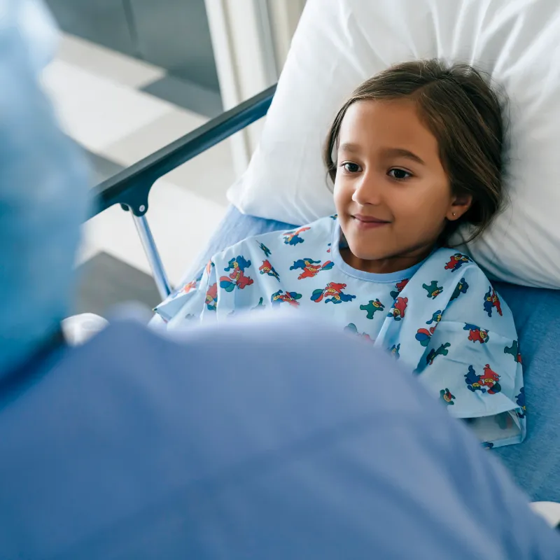 A young child is lying in a hospital bed talking with a health care provider. 