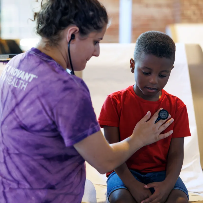 A Novant Health healthcare provider is listening to the heart of a young boy. 