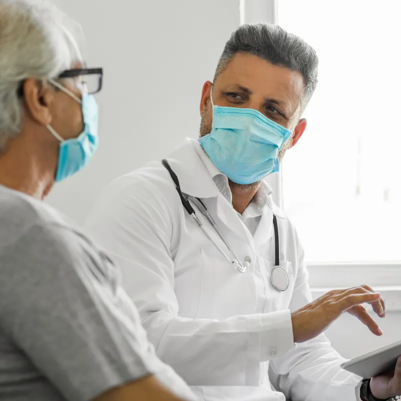 Masked healthcare provider with masked patient in a clinic exam room