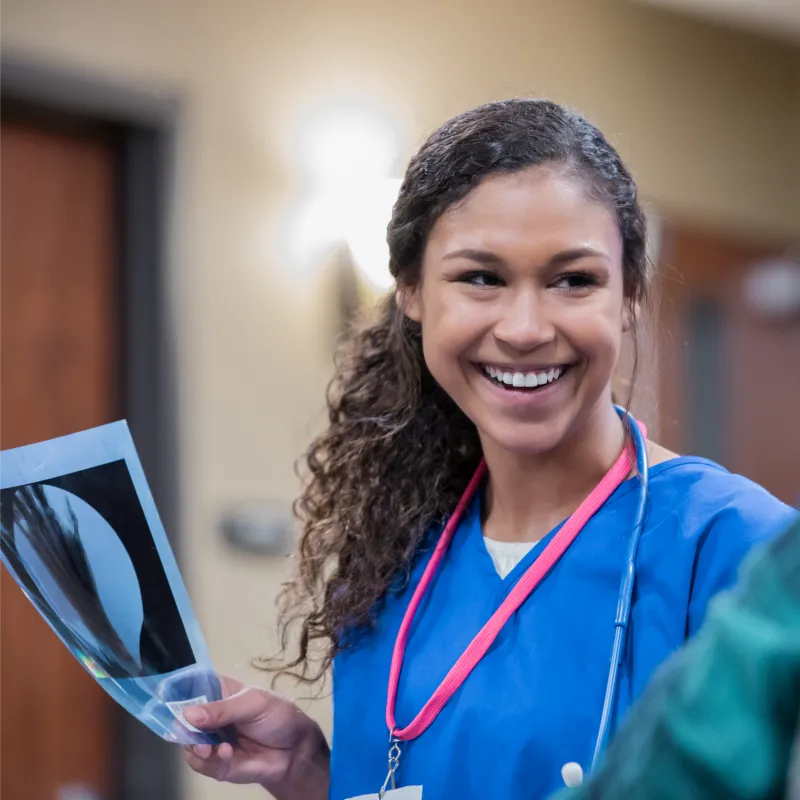 A nurse is smiling at a patient as she holds their imaging scans