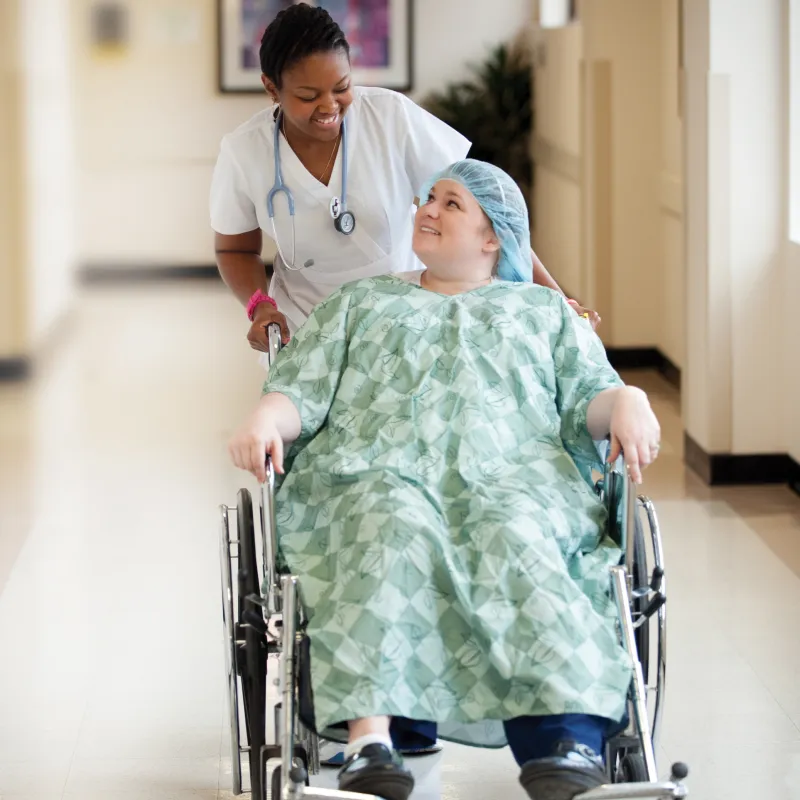 smiling nurse wheels a patient through the halls in a wheelchair
