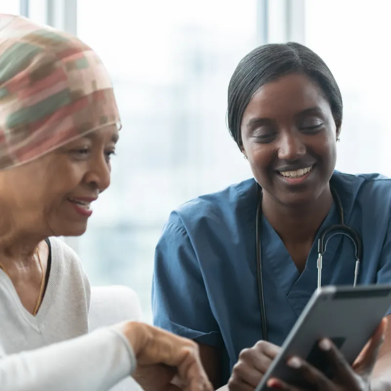 A cancer patient is sitting with a team member reviewing Information on a tablet. 