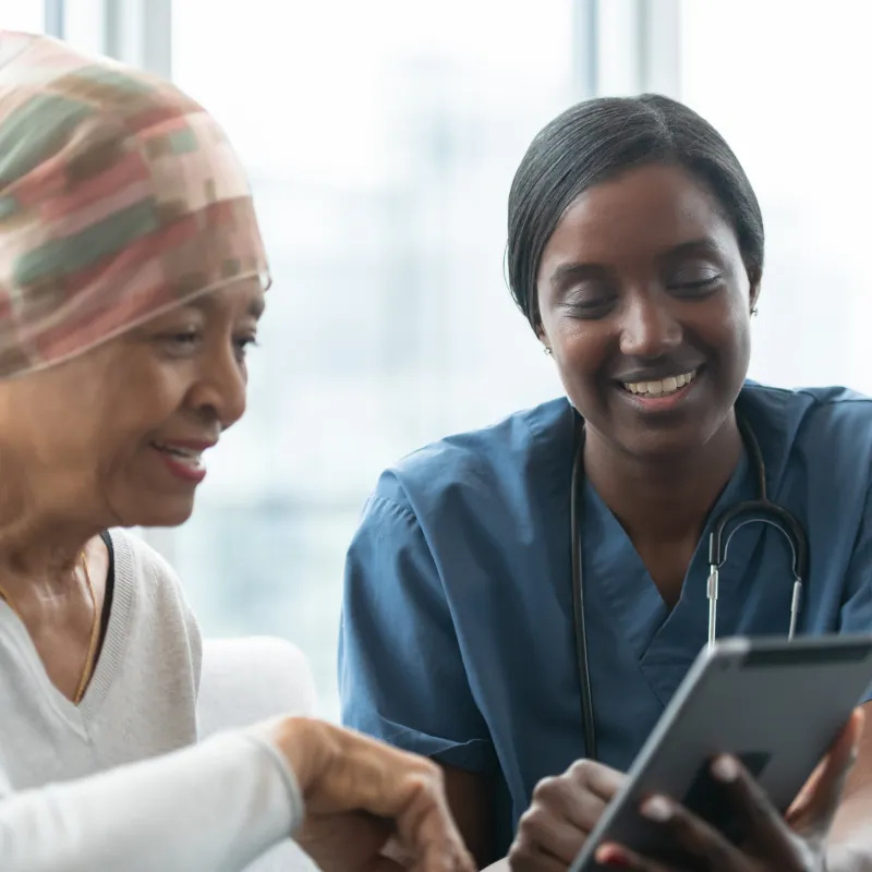 A cancer patient is sitting with a team member reviewing Information on a tablet. A cancer patient is sitting with a team member reviewing Information on a tablet.