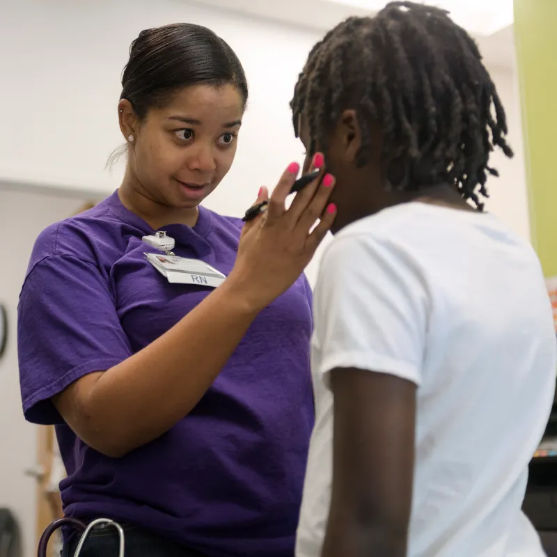 A Novant Health Registered Nurse (RN) is talking with a young child. The RN has a hand placed on the childs face as she talks and looks them in the eye. 