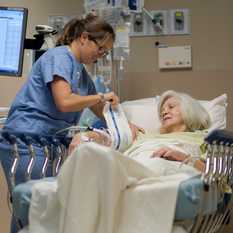 Nurse and patient are in the post-op area of the hospital. The patient is lying in bed, while the nurse wraps a blood pressure cuff around her arm. Nurse and patient are in the post-op area of the hospital. The patient is lying in bed, while the nurse wraps a blood pressure cuff around her arm.