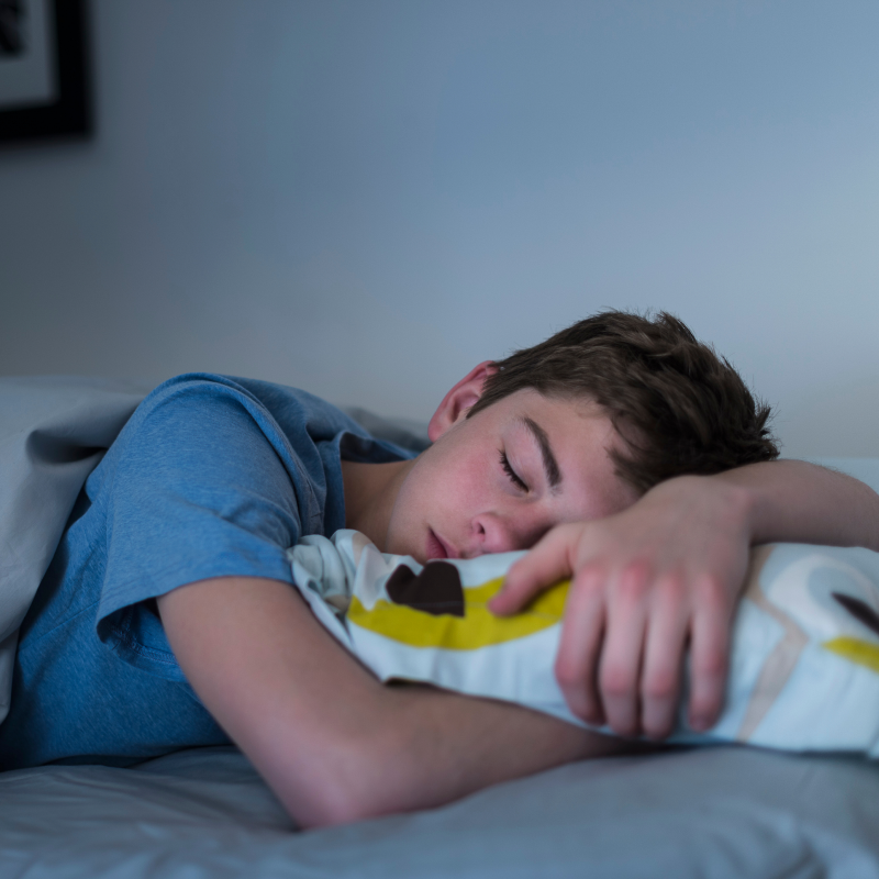 A young teenage boy is sleeping in his bed. 