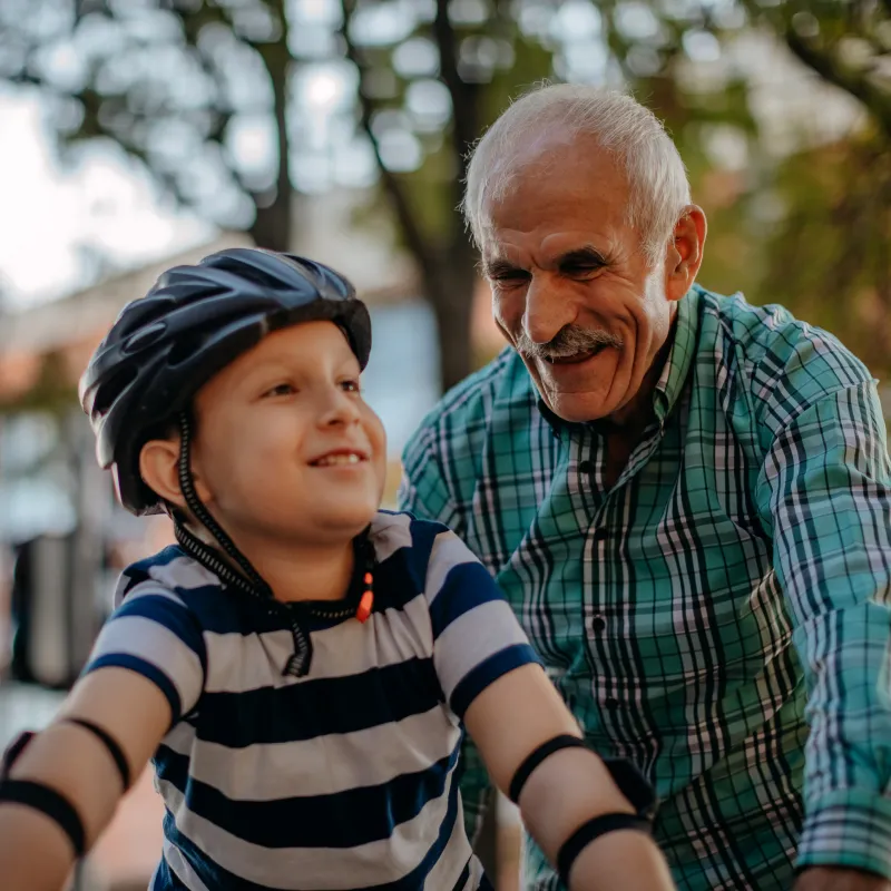 An older man is assisting his grandson as he rides his bike. 