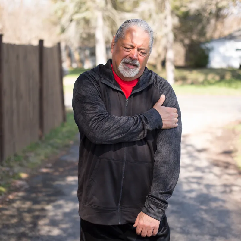 A man grabs his shoulder in pain as he is outside walking a trail