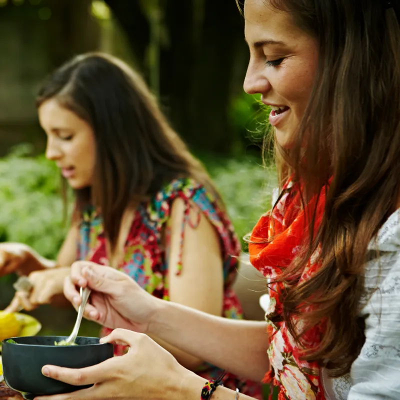 Two women seated at outside dinner table eating and talking. 