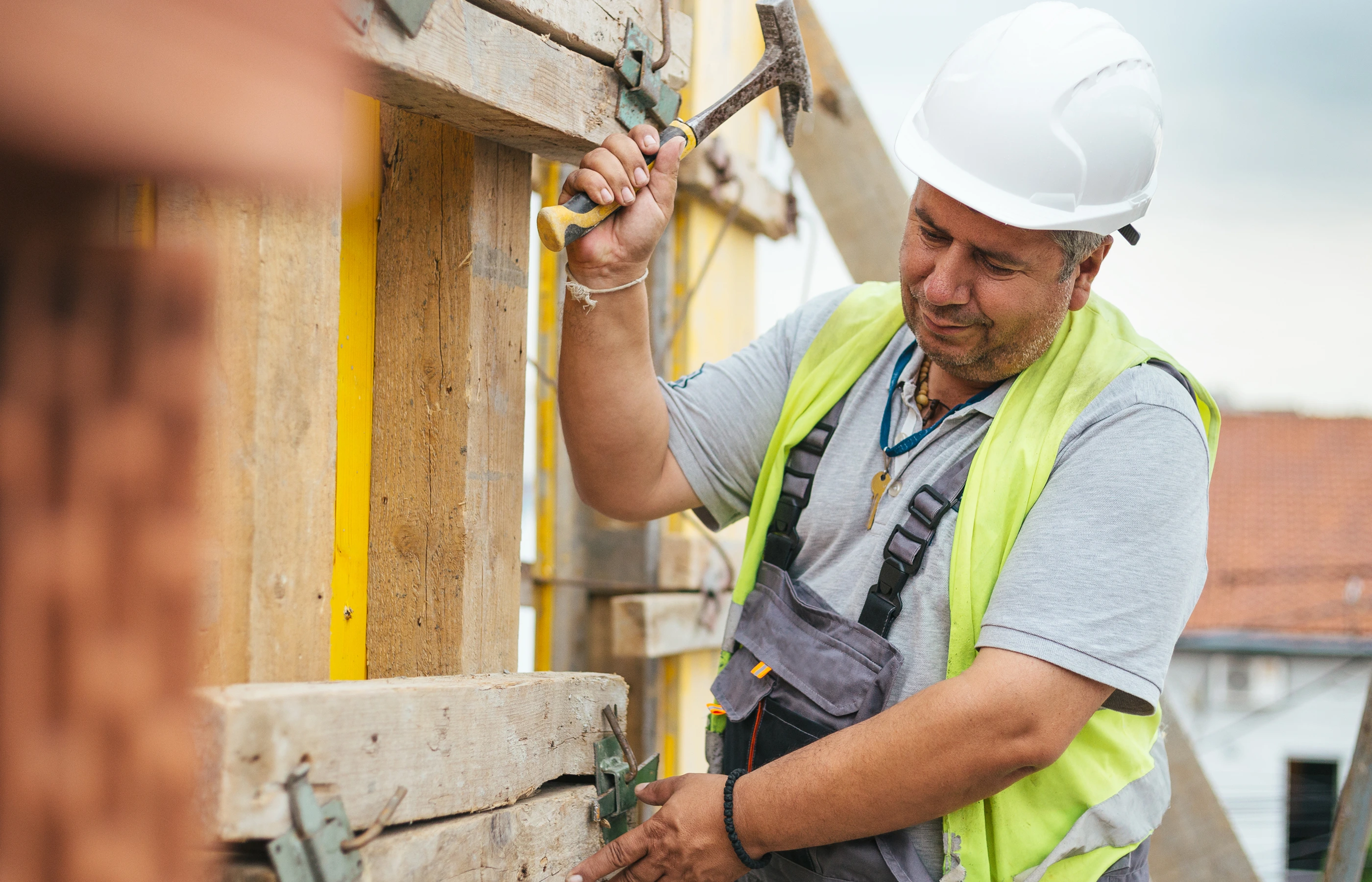 Worker in hardhat and safety vest hammering at a construction site. Worker in hardhat and safety vest hammering at a construction site.